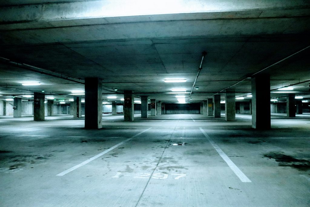 Estacionamiento subterráneo vacío con columnas de concreto, líneas blancas en el piso y luces fluorescentes